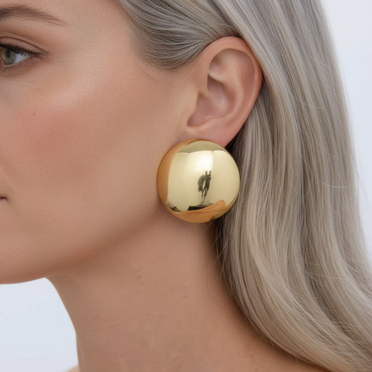 A large gold disc earring held flush against the lobe