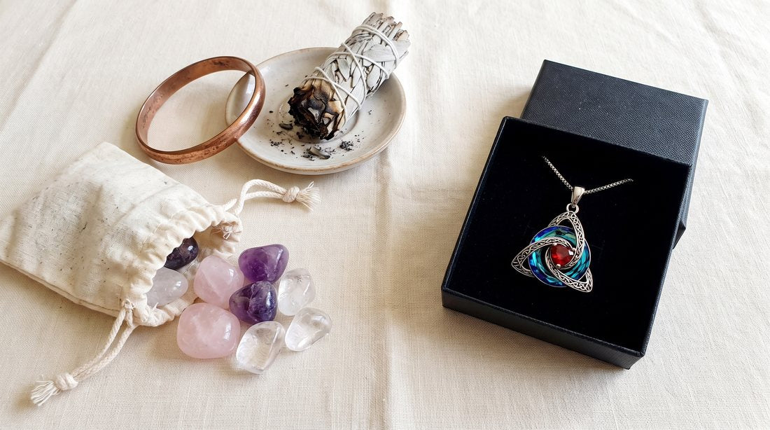 Old crystals, a copper bangle and sage next to the witch knot necklace in its box