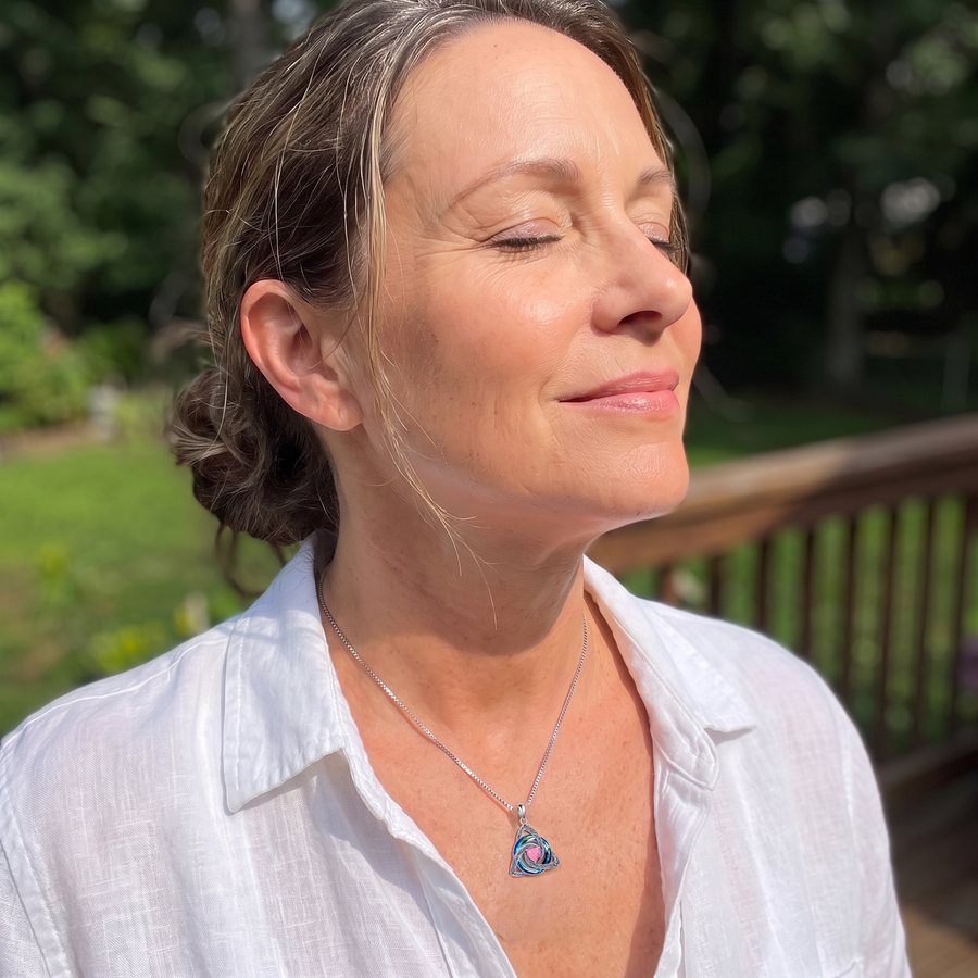 A woman in the sun wearing the necklace, the crystal glowing turquoise