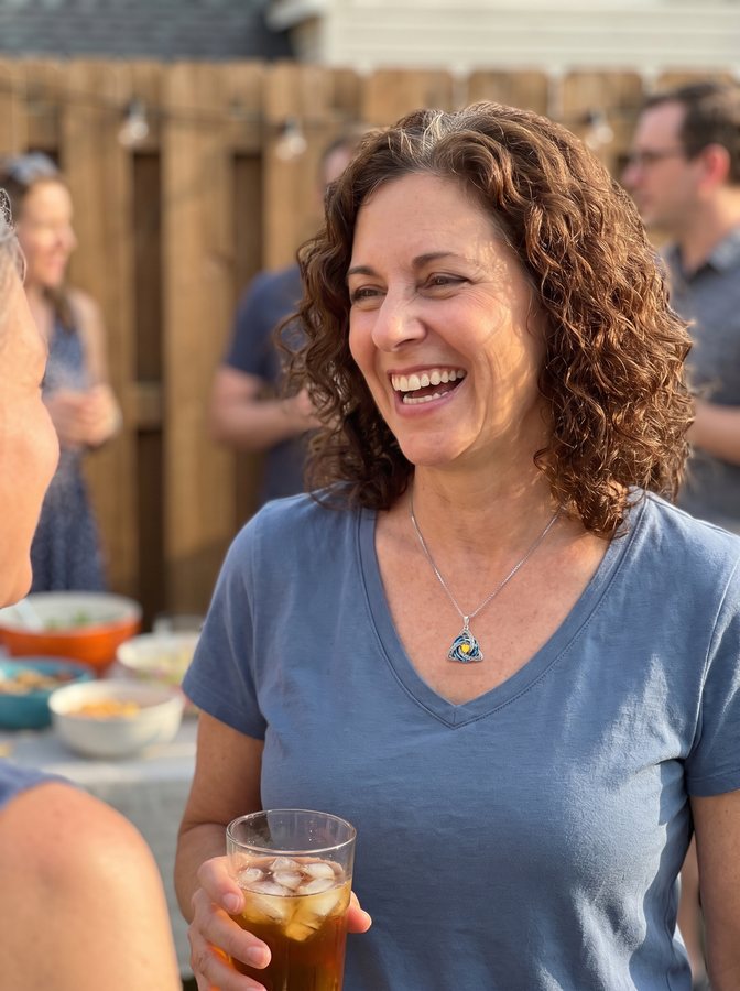 A woman laughing at a backyard party, wearing her necklace