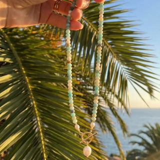 Turquoise Bead Pearl Necklace in gold held up against a palm frond at sunset