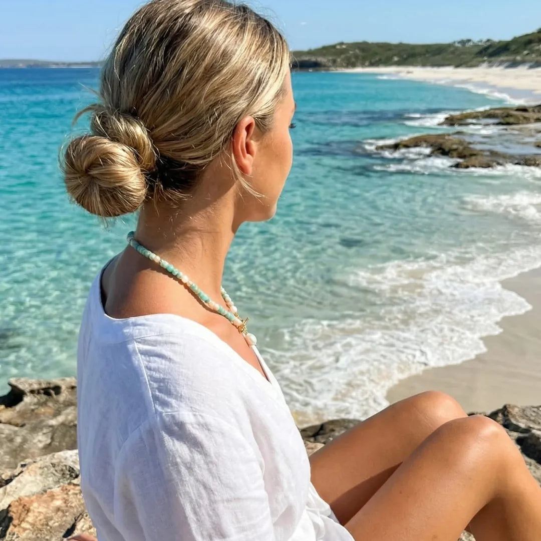 Woman sitting by clear turquoise water wearing the Turquoise Bead Pearl Necklace