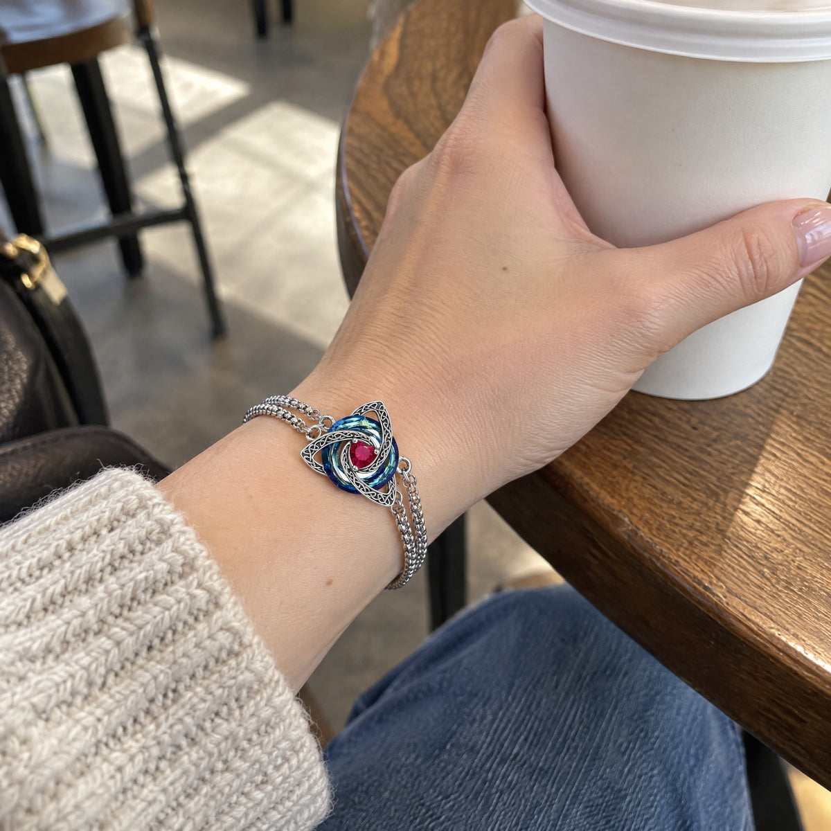 Wrist wearing the witch knot birthstone bracelet, hand holding a coffee cup