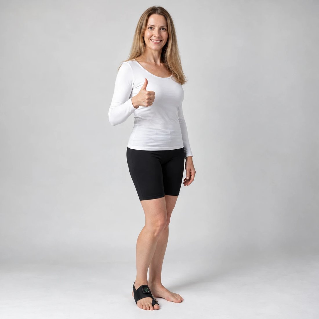 A smiling woman standing barefoot with the Avera EMS support on her foot, giving a thumbs up