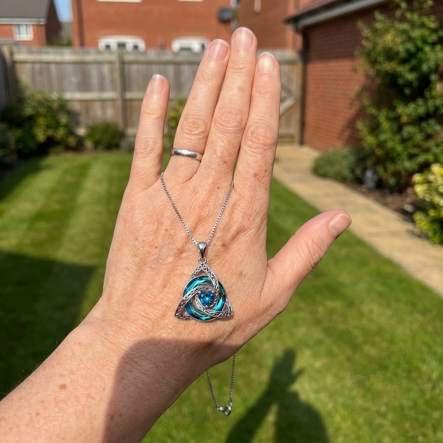 A woman holding the witch knot necklace up in her garden