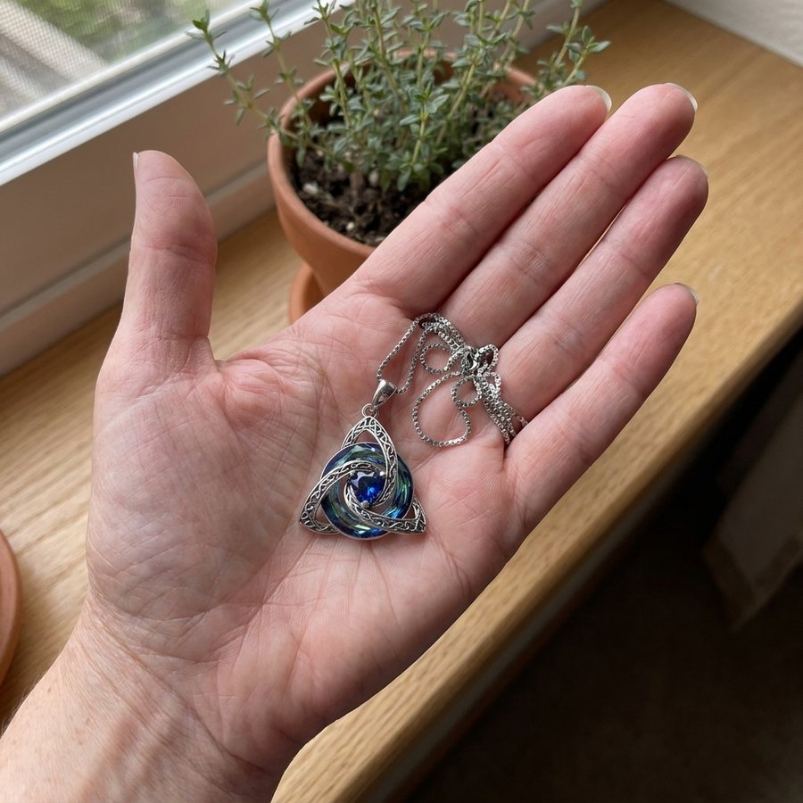 The witch knot pendant resting in an open palm by a window