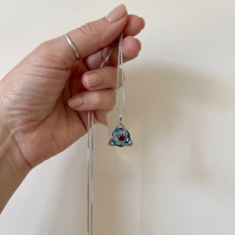 A woman's hand holding up the witch knot birthstone necklace